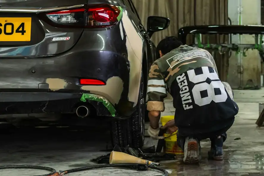 Chapista reparando el paragolpes trasero de un auto gris