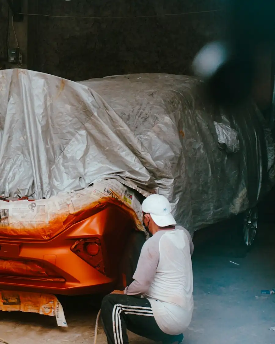 Pintor preparando un auto naranja cubierto con plástico